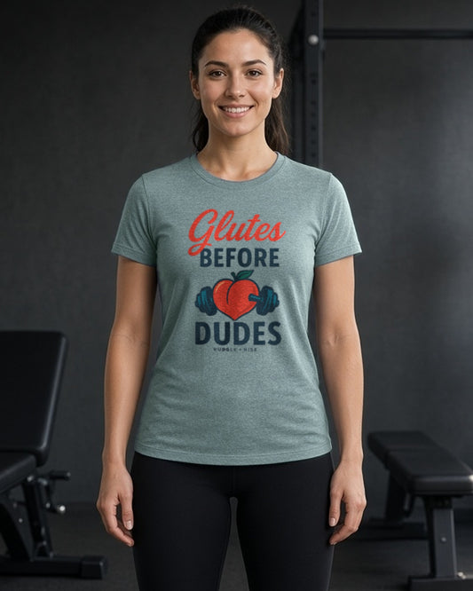 Woman in a gym wearing the Rubble and Rise Glutes Before Dudes tee in Heather Blue Lagoon