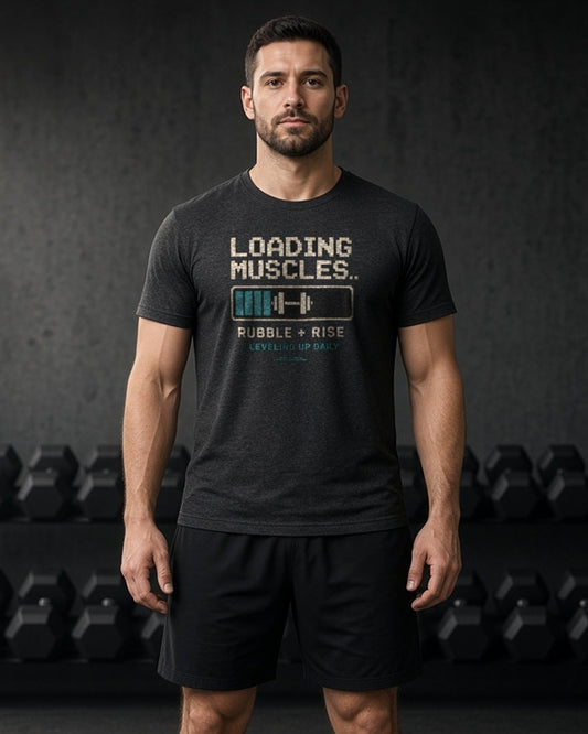 Man in a dark gym wearing the Rubble and Rise Loading Muscles workout tee in Black Heather