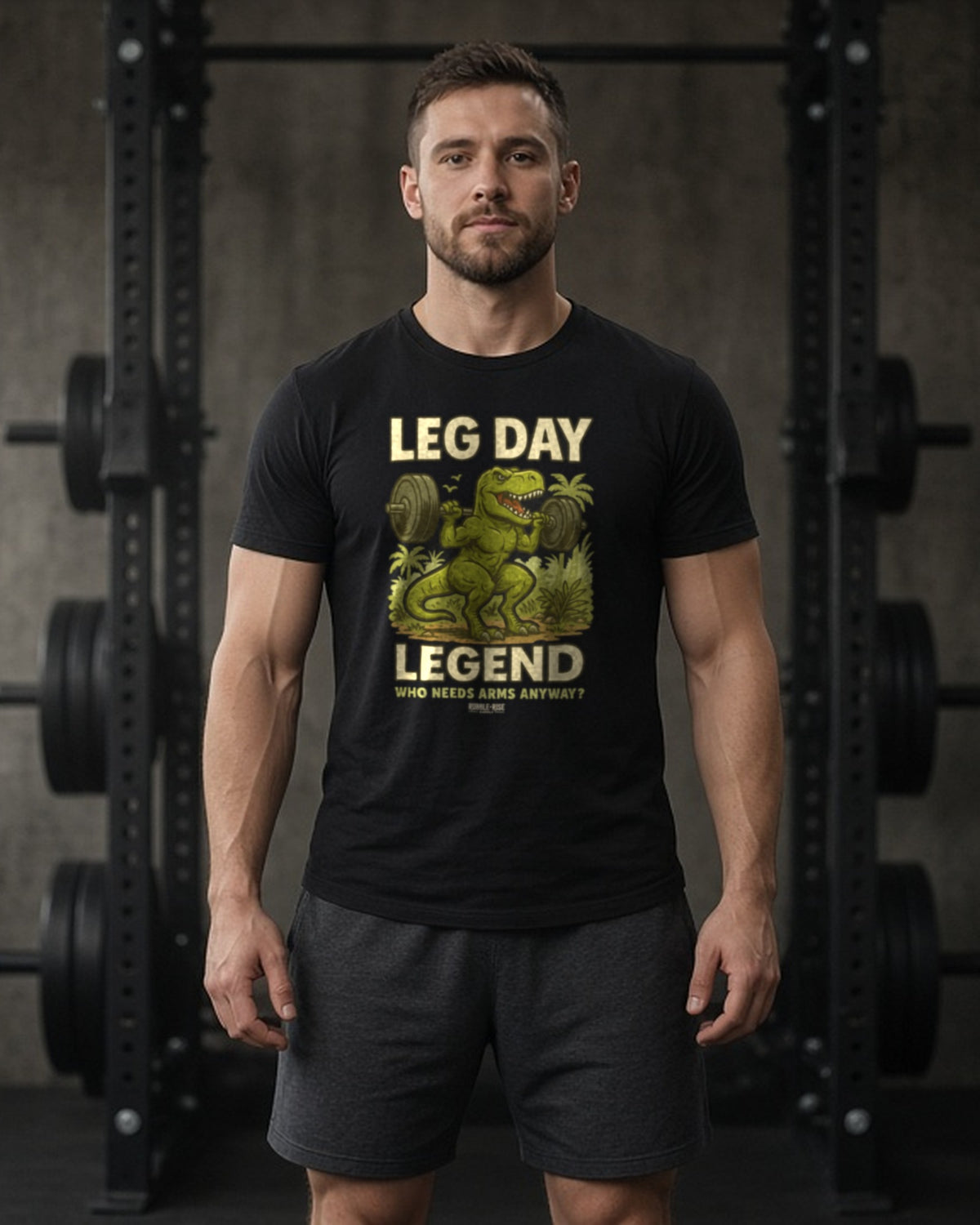 Man in a dark gym wearing the Rubble and Rise Leg Day Legend T-Rex tee in Solid Black Blend